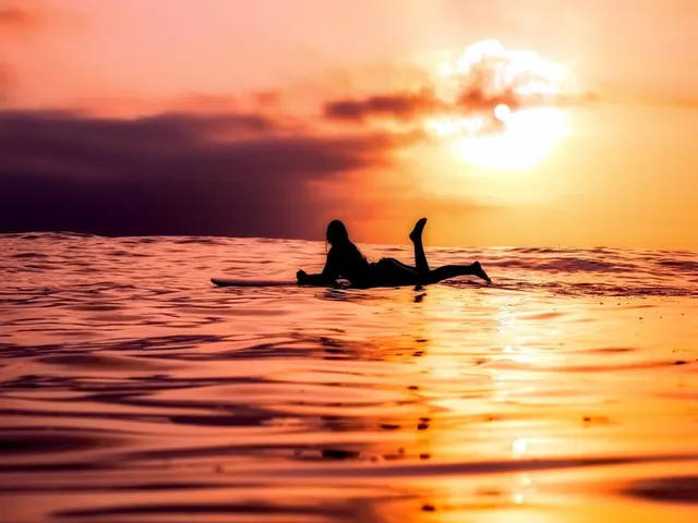 A person resting on a surfboard on calm water at sunset