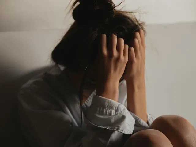 A person sitting against a wall with their head in their hands
