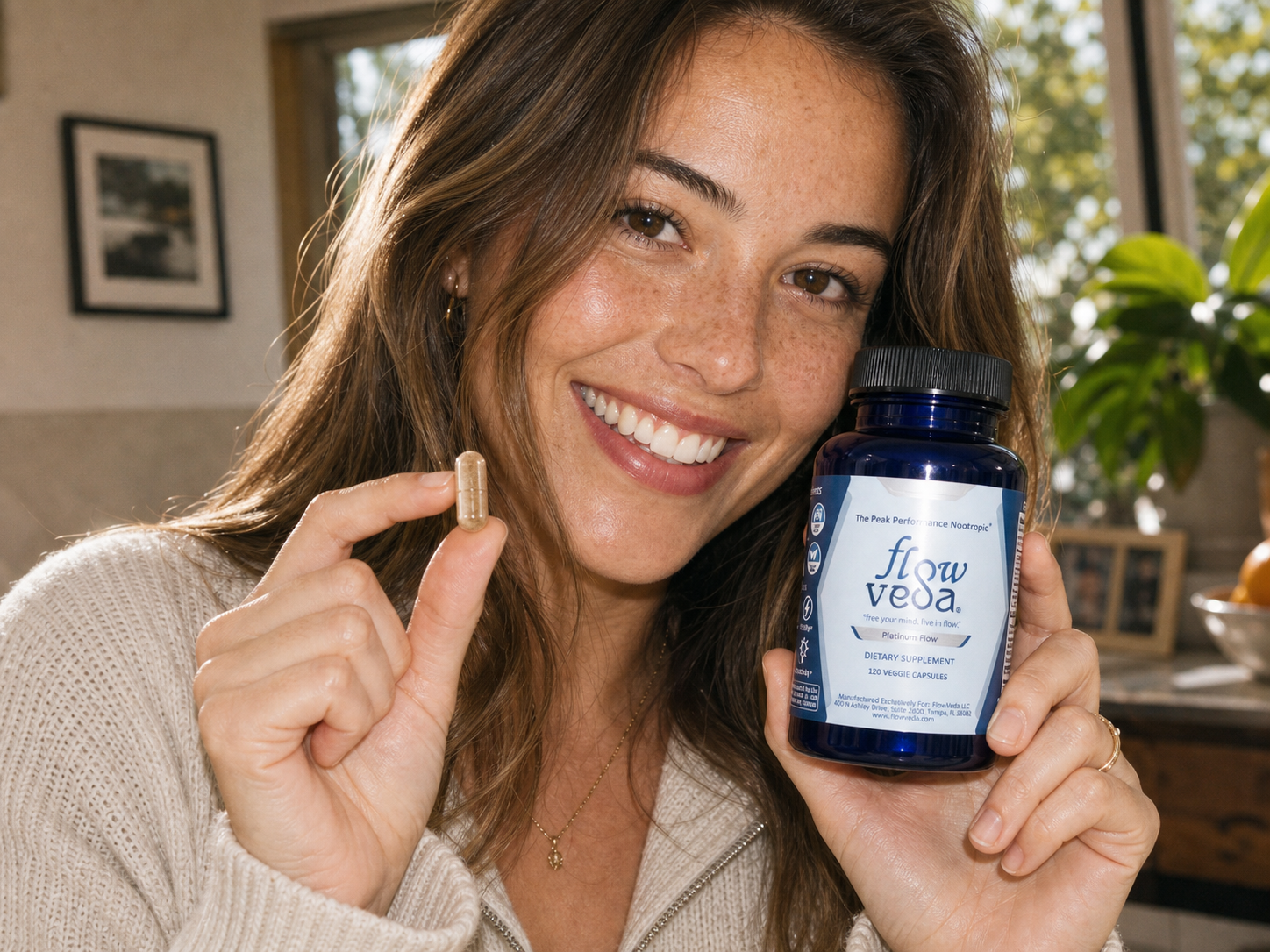 A smiling woman holding a FlowVeda capsule and bottle.
