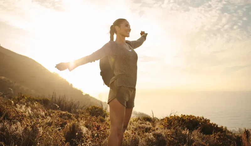 Woman on a mountainside at sunset with her arms open.